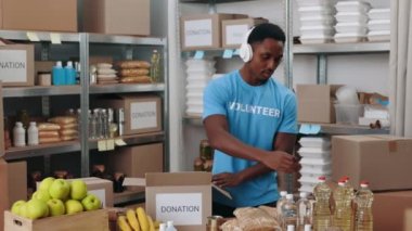 Kulaklıklı Afrikalı Amerikalı adam bağış kutuları paketliyor.