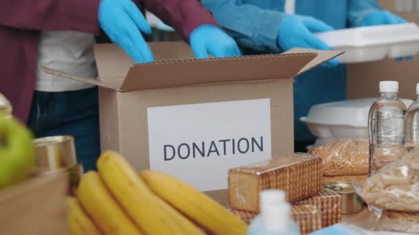 Добровольцы в перчатках упаковывают коробки с едой на благотворительность — стоковое видео