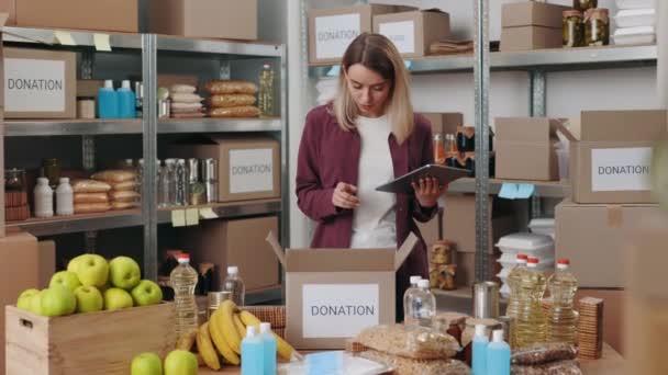 Travailleur de banque alimentaire utilisant la tablette lors de l'emballage des boîtes — Video