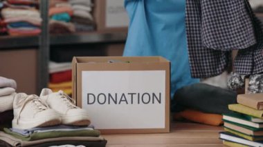 Kadın gönüllü giysileri ayırıp depodaki dolaba koyuyor. İnsani yardım ve bağış konsepti. Kırpılmış görünüm.