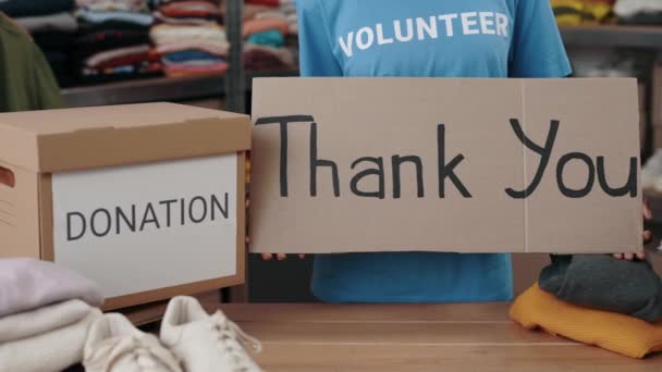 Mujer multirracial sosteniendo pancarta con frase de agradecimiento en la tienda de caridad. Voluntariado que trabaja en la organización y clasificación de ropa donada. De cerca.. — Vídeo de stock