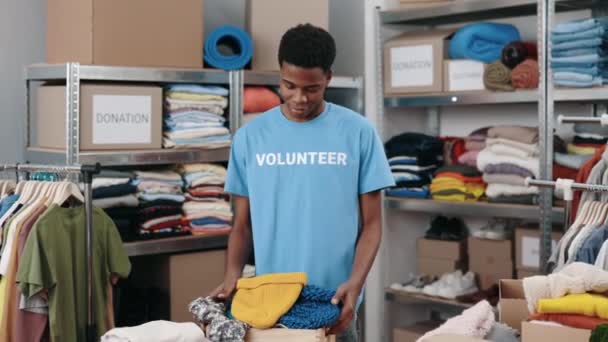 Voluntario masculino multirracial trabajando en el centro de donación y desplegando una caja de armario con ropa. Concepto de ayuda humanitaria y voluntarios. — Vídeo de stock