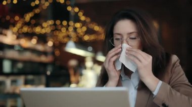 Kafede dizüstü bilgisayarı olan ve peçeteye hapşıran bir kadın.