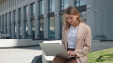 İş kadını bankta oturuyor ve laptopta çalışıyor.