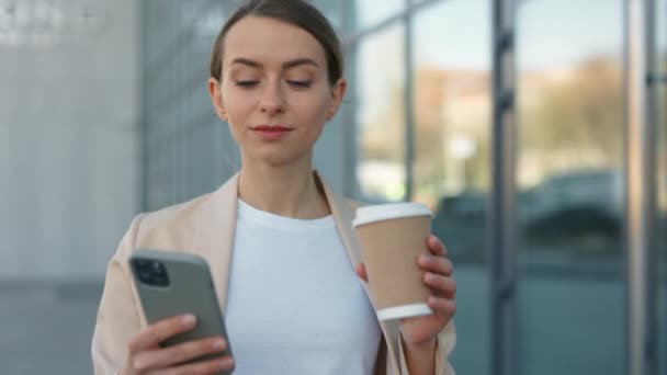拿着智能手机和咖啡杯在办公室附近散步的女人 — 图库视频影像