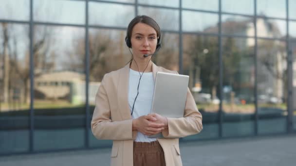 Mujer con auriculares y portátil de pie cerca del edificio de oficinas — Vídeos de Stock