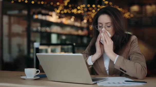 Kobieta dmuchanie nosa w serwetce podczas korzystania z laptopa w kawiarni — Wideo stockowe