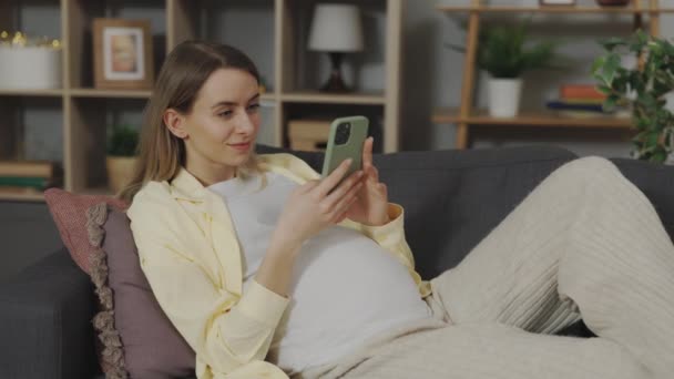 기분좋은 임신부가 소파에 현대의 스마트폰으로 Sms 편하게 미래의 어머니는 집에서 — 비디오