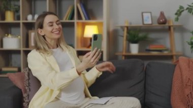 Kanepede oturan mutlu hamile kadın ve görüntülü konuşma sırasında bebeğin ultrason görüntüsünü gösteriyor. Beyaz anne modern akıllı telefonu aile ile çevrimiçi konuşma için kullanıyor..