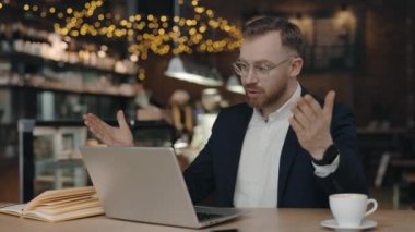 Kahvede görüntülü konferansta gülümseyen iş adamı konuşuyor. Laptop bilgisayarında video görüşmesi yapan yakışıklı bir işçi. Uzak iş yerlerinde jestleri olan erkek profesyonel açıklama projesi