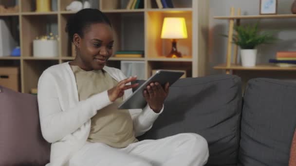 미래의 아프리카 미국인 어머니는 소파에 디지털 태블릿으로 미디어를 둘러보고 있습니다 — 비디오