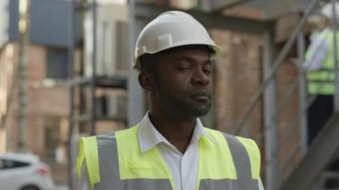 Afro-Amerikan erkek müteahhitin portresi. Açık havada sakin bir şekilde kameraya bakıyor. Büyük inşaat şirketinde çalışan kendine güvenen bir adam..