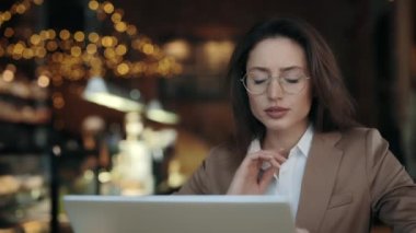 Gözlüklü güzel bir iş kadını ve kafeteryada otururken ağrısı yüzünden boynuna masaj yapan resmi bir ceket. Modern laptop ve bir fincan kahve..