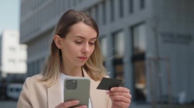 Beyaz kadın girişimci, kredi kartı ve akıllı telefonla açık hava alışverişi yapıyor. İş merkezinin yanında duran başarılı kadın çevrimiçi alışveriş yapıyor.
