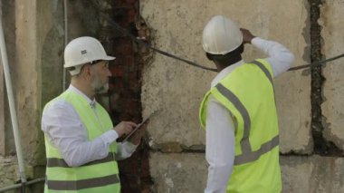 Kafkas meslektaşı dijital tablet üzerine notlar alırken Afrika kökenli Amerikalı bir mimar yeniden yapılanma fikirlerini paylaşıyor. İnşaat duvarının yanında duran iş arkadaşları temiz havada..