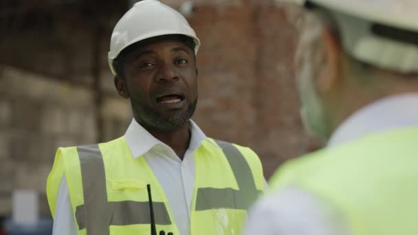 Portret Afrykańskiego Amerykańskiego Budowniczego Twardym Kapeluszu Rozmawiającego Białym Współpracownikiem Placu — Wideo stockowe