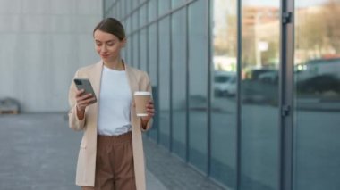 Resmi giyinmiş çekici sarışın kadın dışarı çıkıp kahve içerken modern akıllı telefon kullanıyor. İş, yaşam tarzları ve kahve molası kavramı.