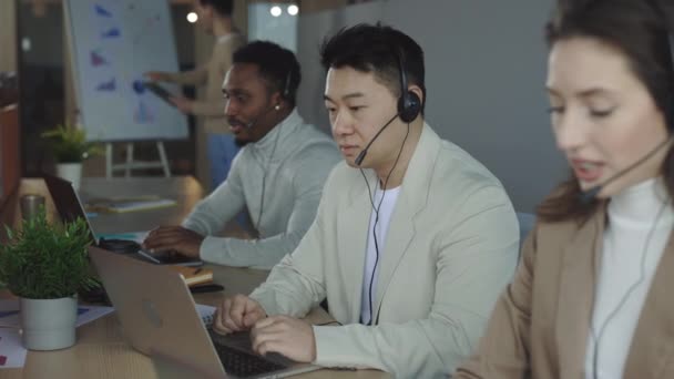 Серьезный Азиатский Работник Мужчина Сидящий Столом Ноутбуком Использующий Гарнитуру Давать — стоковое видео