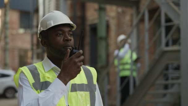 Odpowiedzialny Wykonawca Twardym Kapeluszu Pomocą Krótkofalówki Stojący Pobliżu Placu Budowy — Wideo stockowe