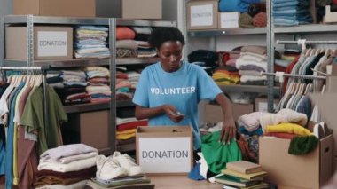 Toplum bağış merkezinde bağışlanan kıyafetleri sıralayan bir gönüllü. Çok ırklı kadın işçiler giysileri katlayıp depodaki dolaba koyuyorlar. İnsani yardım kavramı