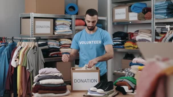 白人は男性ボランティアに靴を選別させ 倉庫の食器棚に入れた 人道支援と寄付の概念 全長表示 — ストック動画