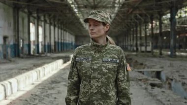 Düşmanlık sonrası yıkıntıların arasında duran üniformalı orta yaşlı kadın portresi. Amerikalı deneyimli asker ciddi bir yüzle kameraya bakıyor..