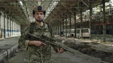 Güvenlik kaskı ve üniformalı tam teçhizatlı profesyonel asker imalat nesnesini koruyor. Elinde siyah makineli tüfekle büyük yetkili bir fabrikada yürüyen kendinden emin bir adam..