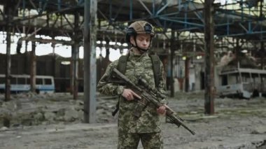 Eğitimli bir asker kadın elinde otomatik tüfekle kameraya bakıyor. Savaş eğitiminden sonra eski harabe bitkilerin üzerinde poz veren orta yaşlı kadın portresi..