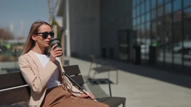 视力受损的妇女坐在商务中心附近的长椅上 喝着热咖啡 身穿黑色眼镜的白种人年轻女性 在户外休闲地穿衣 — 图库视频影像