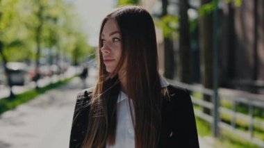 Ofis merkezinin yanındaki güneşli sokakta duran mutlu esmer iş kadını portresi. Başarılı bir girişimci resmi giyinmiş, yüzünde gülümsemeyle kameraya bakıyor..