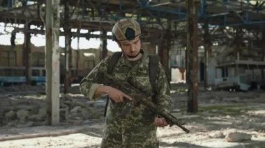 Askeri üniformalı vatansever askerin portresi ve terk edilmiş bir tesiste dururken elinde silah tutan koruyucu miğfer. Kafkasyalı cesur adam kameraya bakıyor. Gözlerine güvenerek..