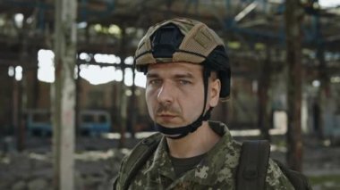 Güvenlik kaskı ve üniformalı korkusuz bir savunucunun portresi yok edilmiş bir tesiste tek başına dikilirken sakin bir yüzle kameraya bakıyor. Cesur kahraman, savaş ve savunma kavramı.