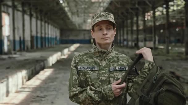 美国女兵背着背包行走在被毁的工厂里 多年战争后 身穿制服 头戴帽子的有信心的爱国妇女返回家园 — 图库视频影像