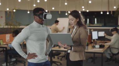 Afrika kökenli Amerikalı iş adamı, sanal gerçeklik simülatörü kulaklığını test ediyor ve havada el kol hareketi yapıyor. Bu arada bayan meslektaşı da el hareketlerini analiz ediyor ve bir dizüstü bilgisayarda kayıt yapıyor. Ofiste çalışanlar