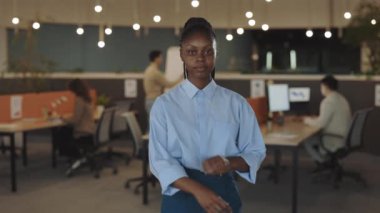 Genç Afro-Amerikan yakışıklı iş kadını modern ofiste kollarını kavuşturarak kameraya bakıyor. Ofis odasındaki kadın portresi. Halk ve iş
