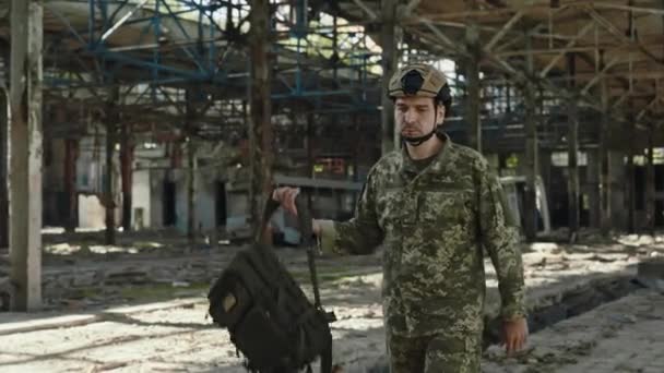 勇敢的高加索人 身穿迷彩服 头戴防护头盔 背着背包行走在被毁的工厂上 战争期间执行防卫任务的士兵 — 图库视频影像