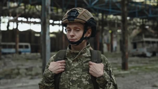 身着战斗服 头戴安全帽的女兵手持军事背包的画像 自信的女人站在被毁的工厂里看着镜头 — 图库视频影像