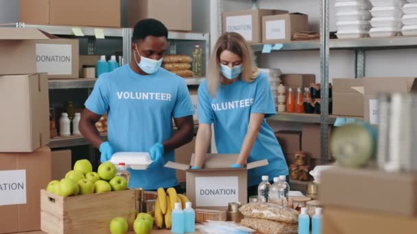多文化志愿者戴着口罩和手套 同时将食物装在纸盒中 供慈善机构使用 合作帮助有需要的人的青年男女在大脑皮层病毒大流行期间 — 图库视频影像