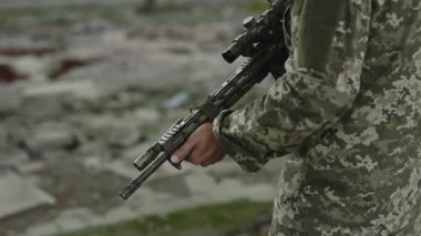 Erkek asker üniforması içinde modern saldırı tüfeği tutarken arka planda fabrikada dikilirken. Silahlı kuvvetler ve nitelikli askeri eğitim kavramı.