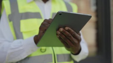 İnşaat alanının yanında dijital tablet kullanan mimar ellerini kapat. Tanımlanamayan Afro-Amerikan inşaatçı, tuğla duvarın arka planıyla çizimleri kontrol ediyor..