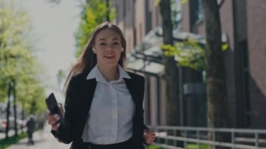 Kulaklıklı bayan ofis çalışanı sokakta ritmik dans ederken en sevdiği şarkıların tadını çıkarıyor. İş merkezinin yakınında boş vakit geçirmek için akıllı telefon kullanan resmi giyinmiş beyaz bir kadın..