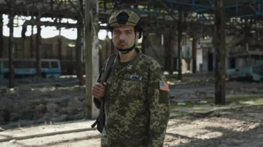 Amerikan ordusundan özgüvenli bir subayın portresi, sırt çantasıyla terk edilmiş çelik fabrikasının arasında duruyor. Güvenlik kaskı ve kamuflaj üniformalı bir asker ciddi bir yüzle kameraya bakıyor..