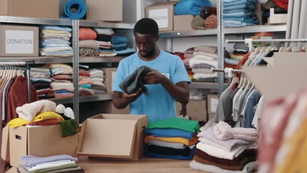 Homem Afro Americano Armazém Enquanto Classifica Repete Roupas Para Doações — Vídeo de Stock