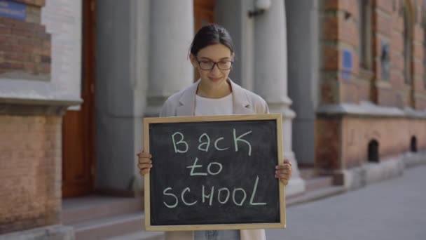 Female Teacher Standing Outdoor Looking Camera Holding Board Text Back — Vídeos de Stock