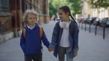 İlkokulda el ele tutuştuktan sonra sırt çantalı mutlu çocuklar. Beyaz erkek ve kız okul bahçesinde yürüyorlar. Öğrenme ve ilk aşk kavramı