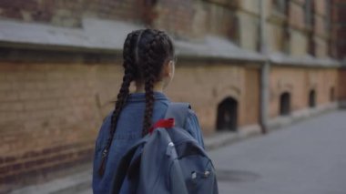 Back view of little girl walking around the street near school in jeans jacket. Child comes back from school. Happy childhood concept