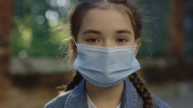Little smart girl standing on street in surgery mask turn around looking at camera close up. Healthcare covid concept