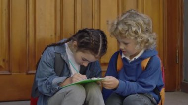 Little schoolgirl make some notes outdoor. Boy looking at girl sitting near his first love and holding her note. Relations and education concept