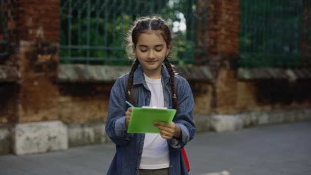 Cute Little Girl Schoolbag Writing Notes Smiling Looking Camera Outdoors — Stockvideo