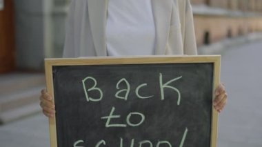 Woman arms holding and raising schoolboard with text message back to school on street close up. Education concept. Close up